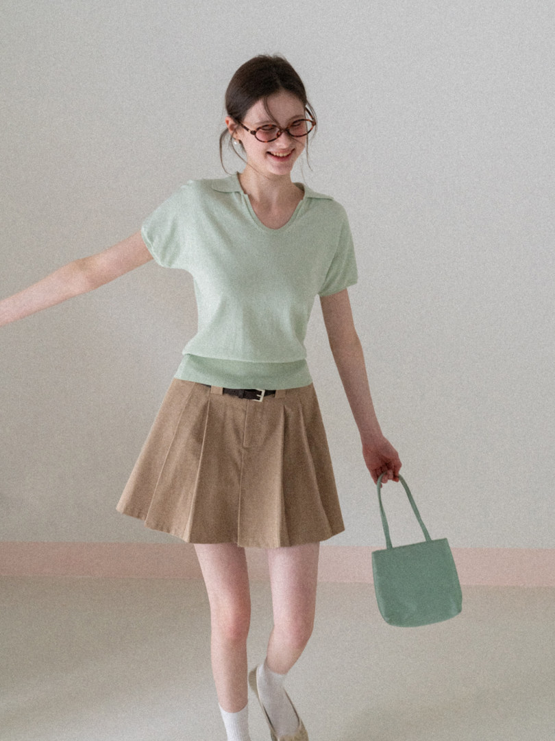 Model wearing a mint short-sleeve top with a beige pleated skirt and small tote bag