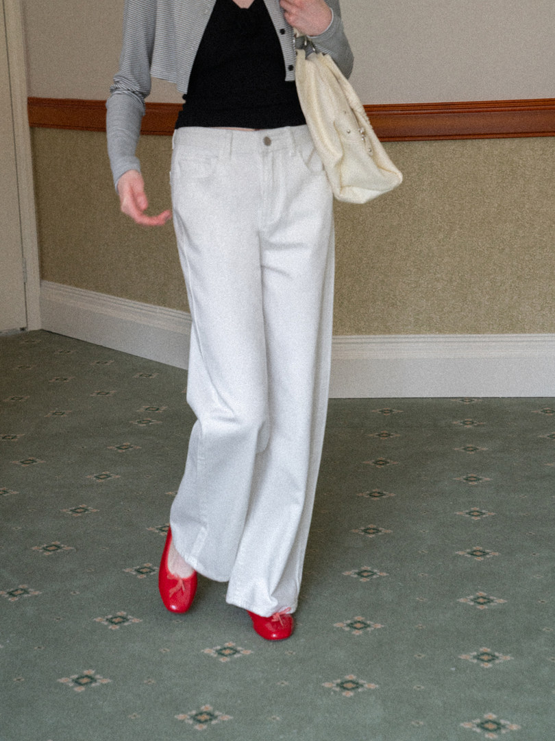 Person wearing white wide-leg pants with a black top, gray cardigan, red flats, and a cream shoulder bag