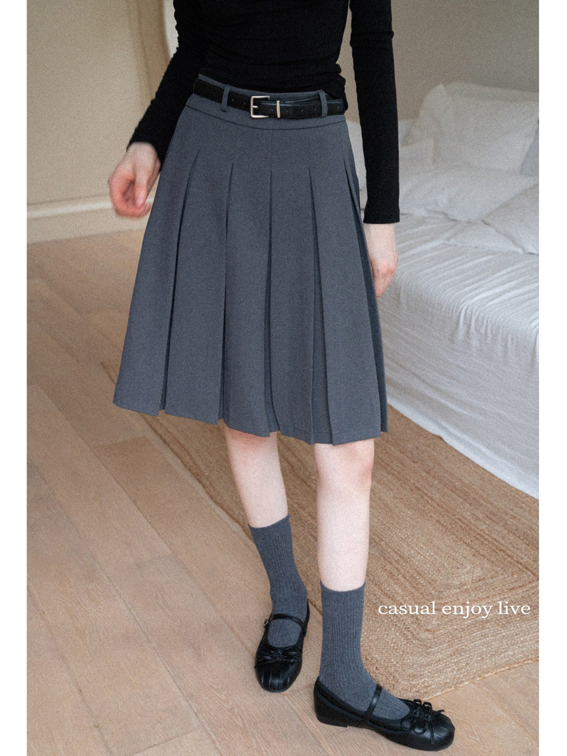Model wearing a pleated gray skirt with a black top, belt, socks, and flats