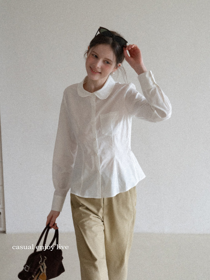 Model wearing a white collared blouse with beige pants and holding a black handbag