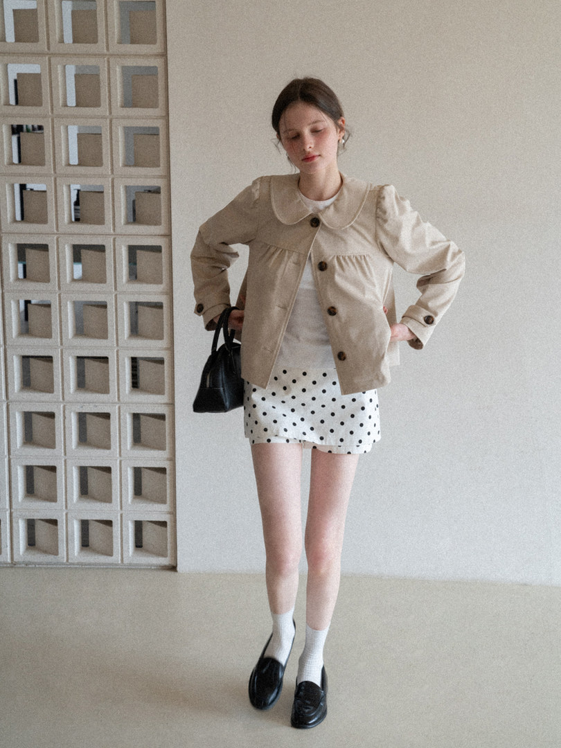 Model wearing a beige cropped jacket with a polka dot mini skirt, black handbag, and loafers