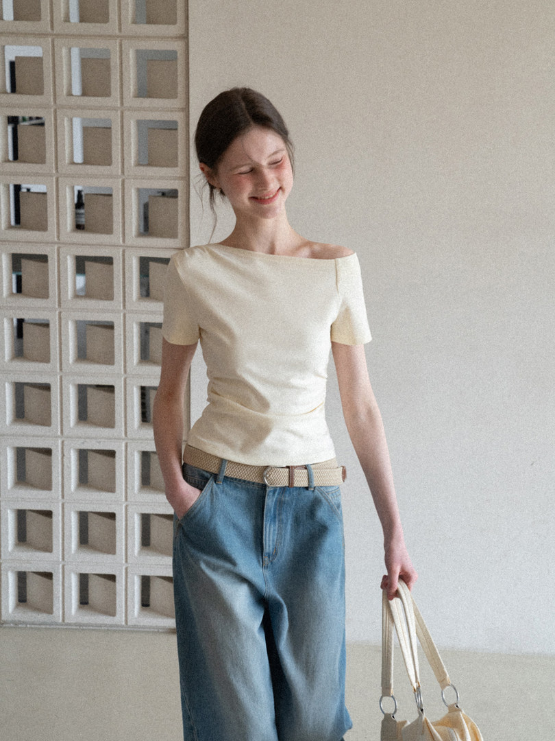 Woman wearing a cream off-shoulder top with blue jeans and carrying a light tote bag