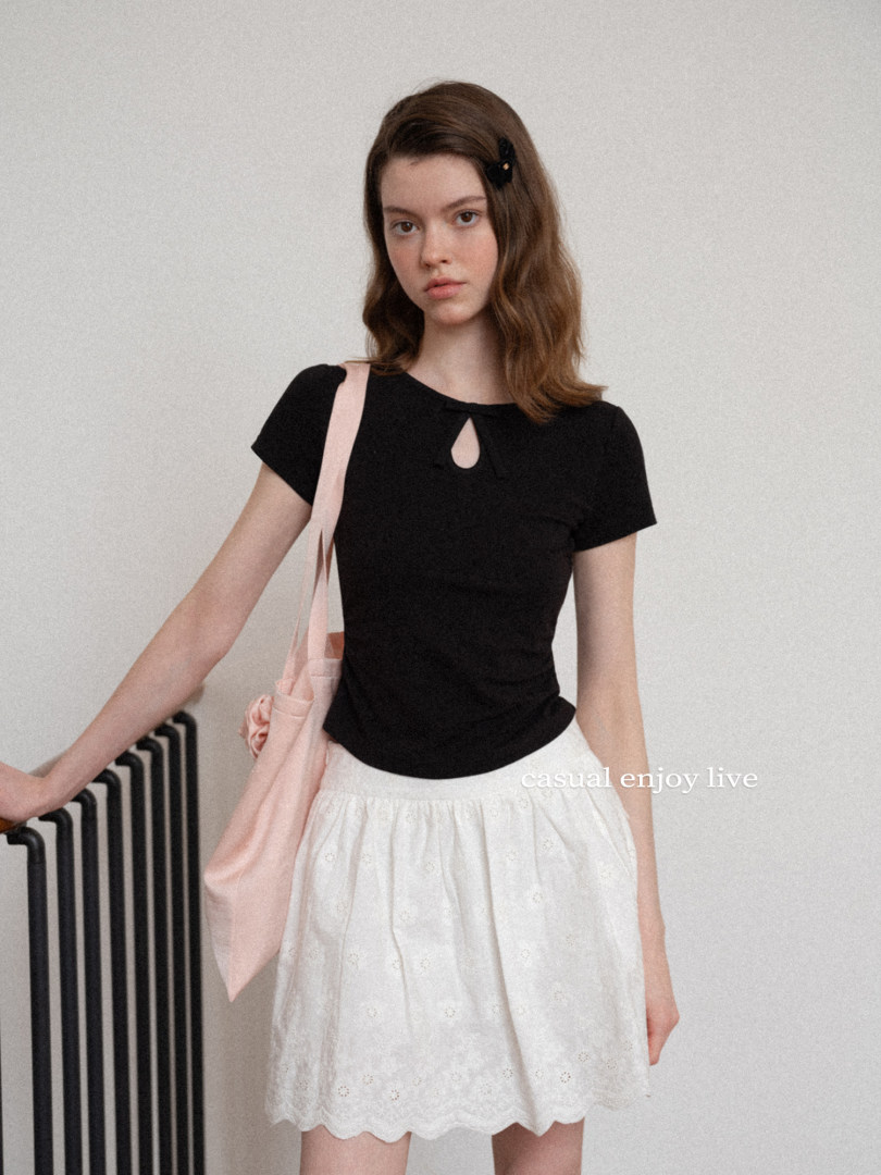 Model wearing a black fitted top with a white skirt and pink shoulder bag