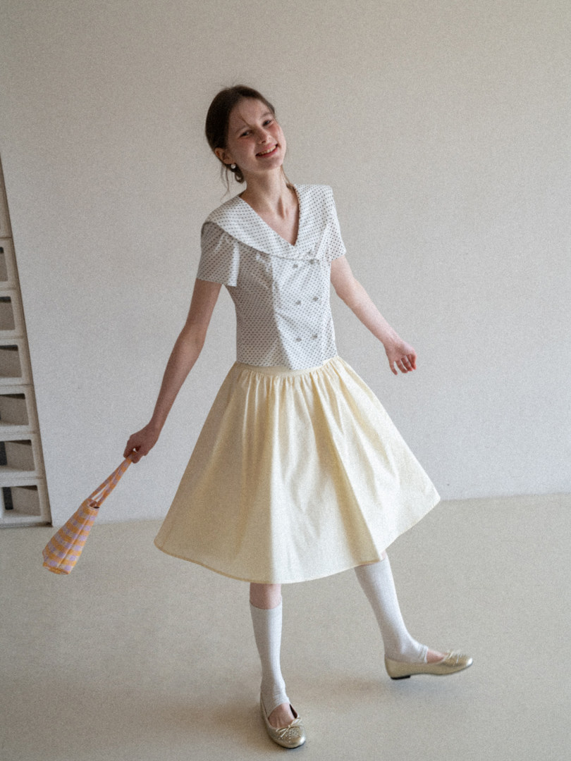 Woman wearing a white patterned sailor-style top with a pale yellow skirt and flats
