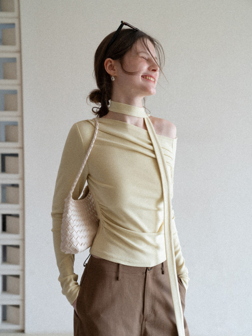Woman modeling a pale yellow off-shoulder top with brown pants and a woven shoulder bag