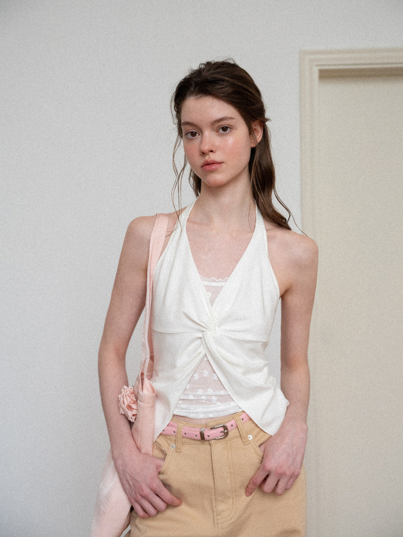 Model wearing a white halter top with beige pants and a pink belt