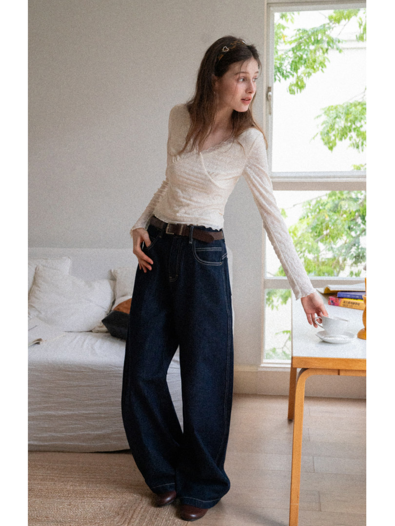 Woman modeling a cream long-sleeve top with dark wide-leg jeans indoors