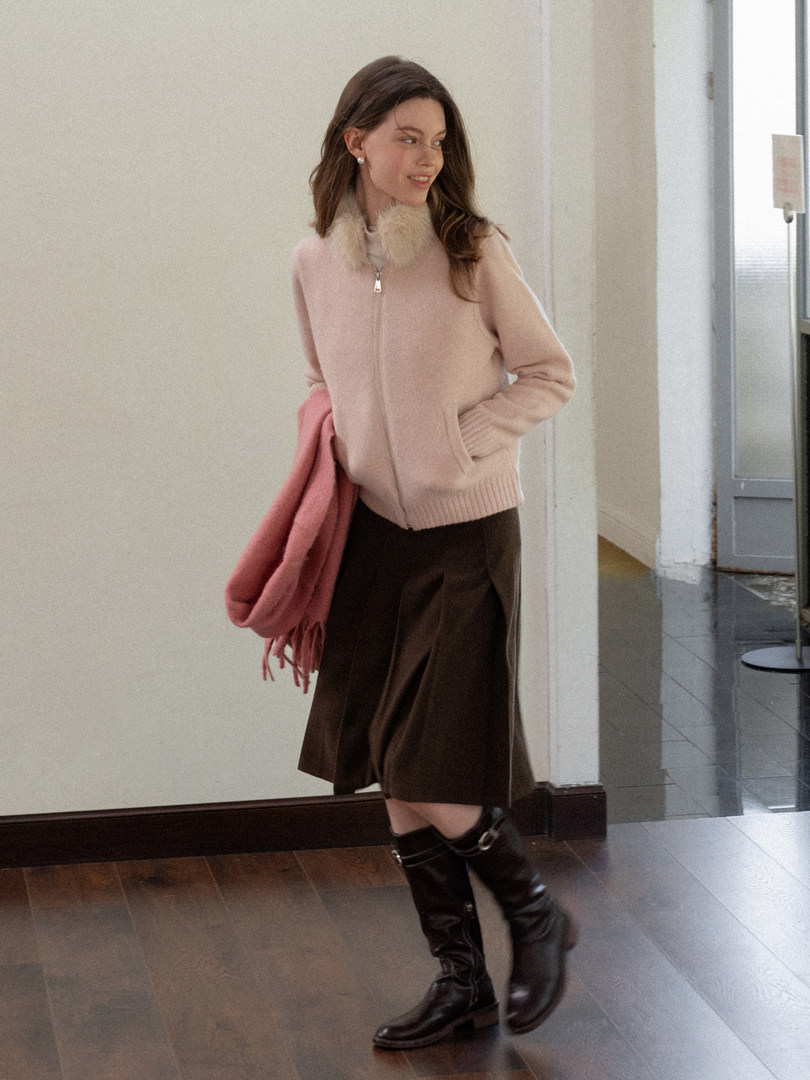 Woman wearing a pink zip-up sweater, brown skirt, and black knee-high boots
