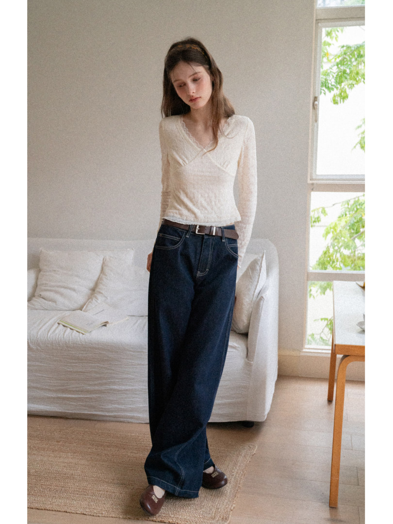Model wearing a white long-sleeve top and dark wide-leg jeans indoors.