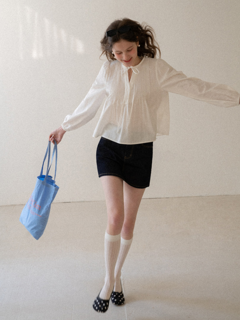 Woman wearing a white blouse, black shorts, and knee-high socks while holding a blue tote bag
