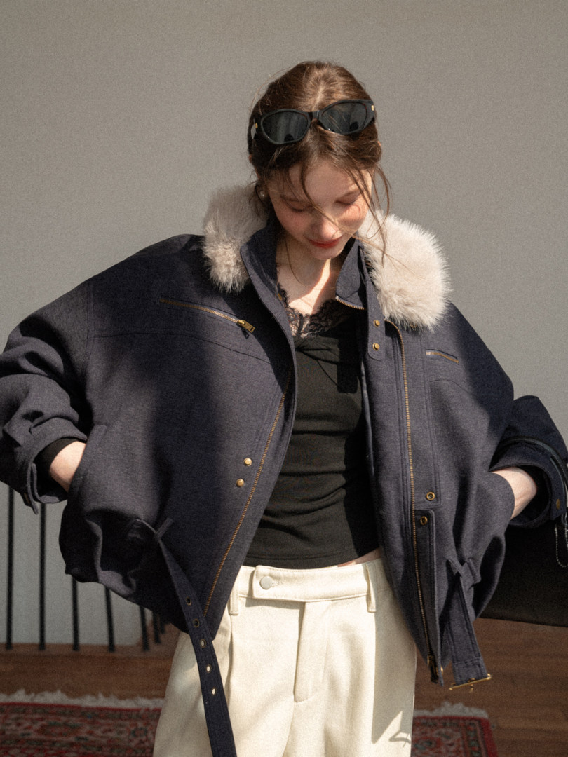 Model wearing a dark oversized jacket with faux fur collar