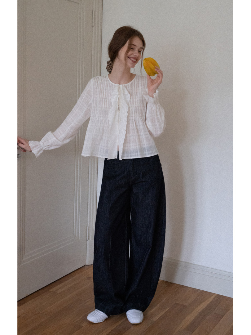 Model wearing a white long-sleeve blouse and dark wide-leg pants