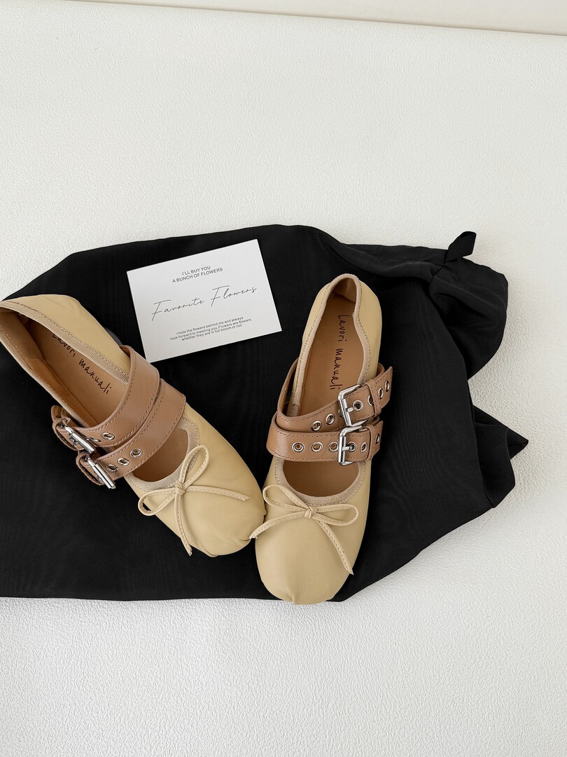 Pair of beige and brown flat shoes with buckle straps and bows on a black cloth