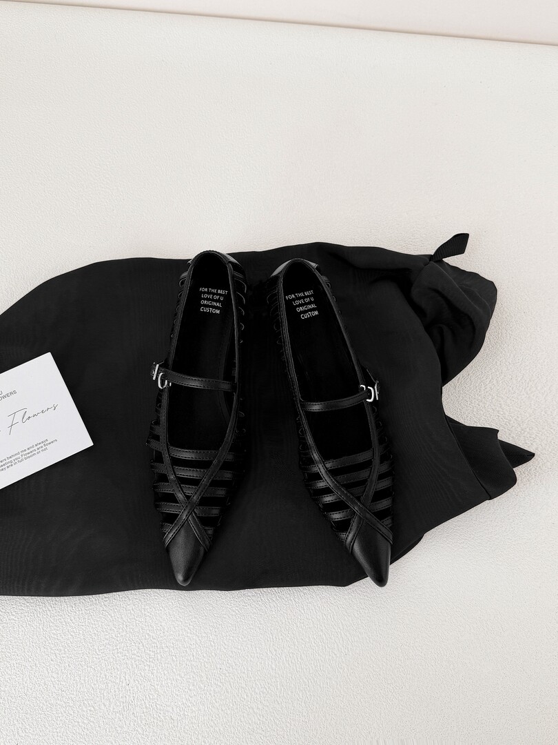 Black pointed-toe strappy flat shoes displayed on a black cloth background