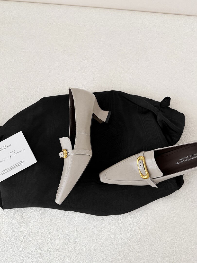 Pair of light gray pointed-toe loafers with gold buckle details on a black garment
