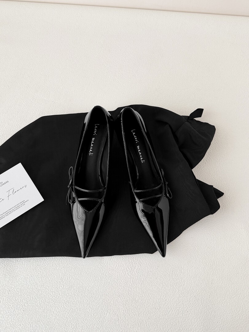 Black pointed-toe patent leather flats displayed on black fabric
