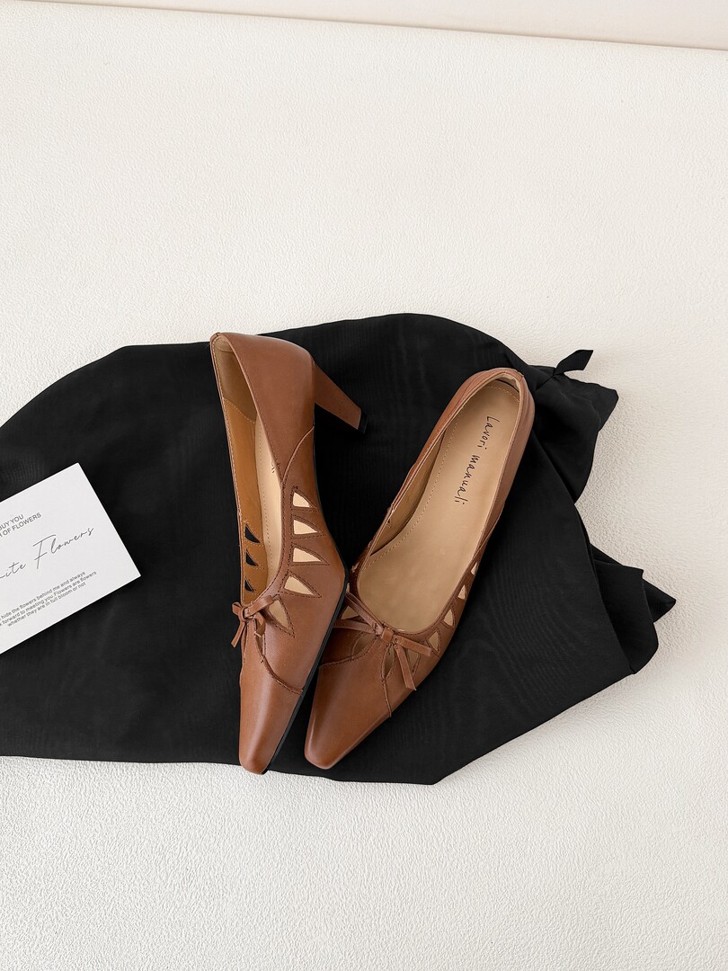 Brown pointed-toe heeled shoes with cutout details laid on black fabric