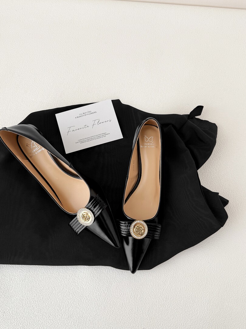 Black pointed-toe flats with gold embellished buckles on a black fabric background