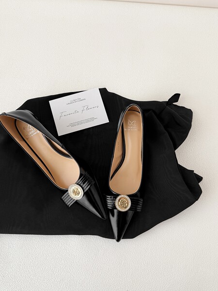 Black pointed-toe flats with gold embellished buckles on a black fabric background
