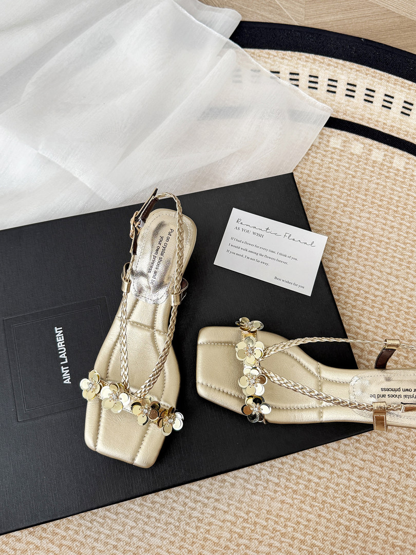 Gold embellished flat sandals displayed on a box with packaging card