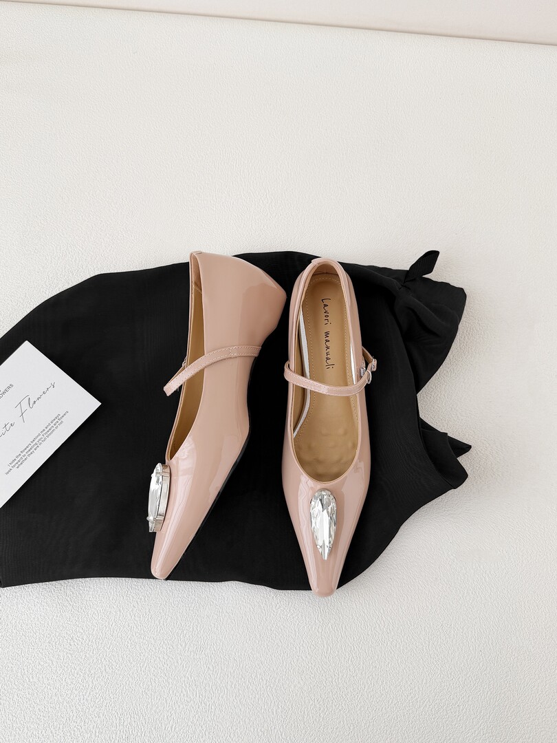Pair of blush pink pointed-toe heels with crystal embellishments displayed on black fabric