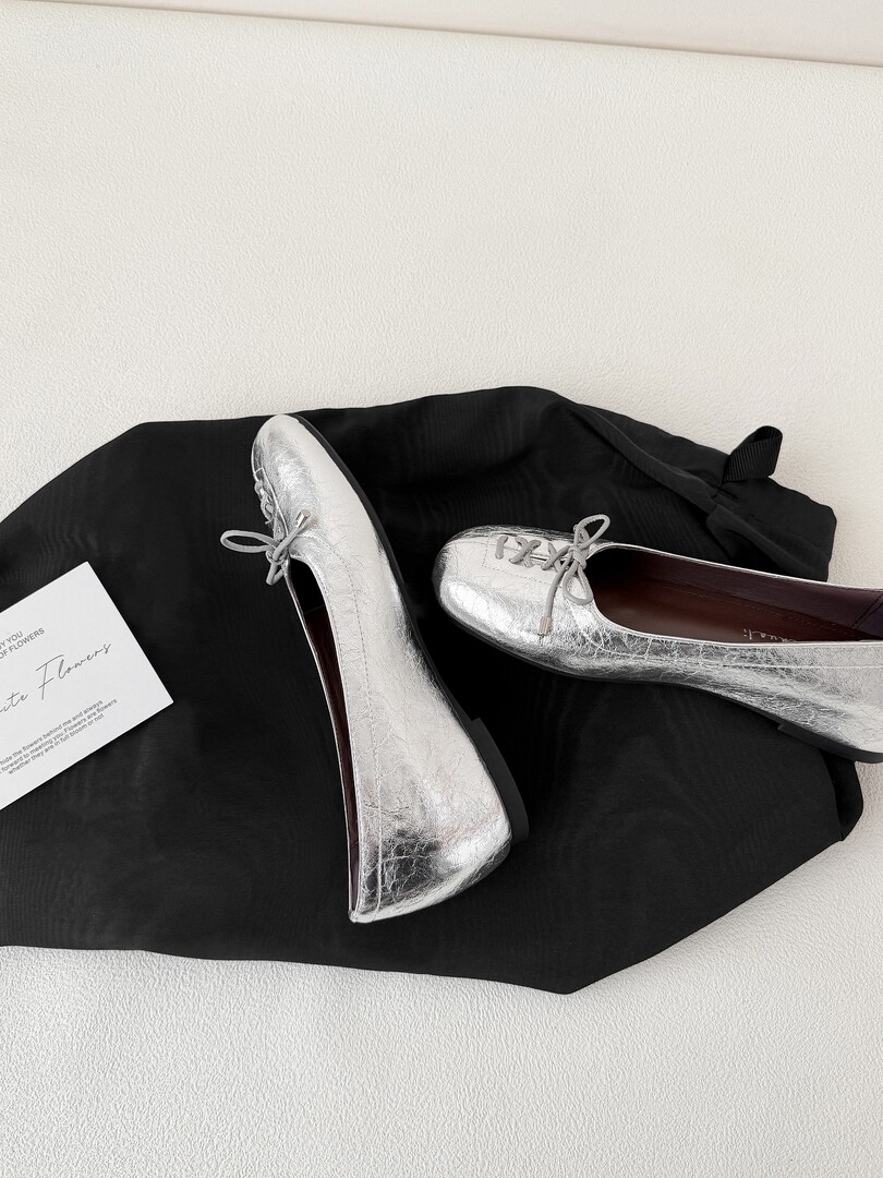 Pair of silver metallic flats laid on a black fabric surface