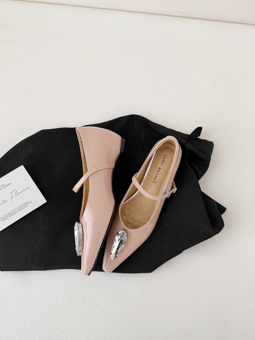 Pair of blush pink pointed-toe slingback flats with crystal embellishments on a black background