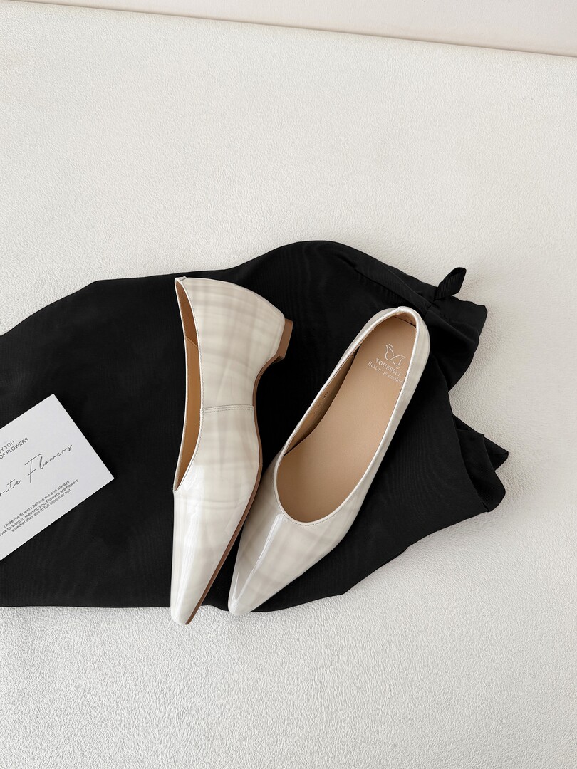 White pointed-toe flats displayed on black fabric