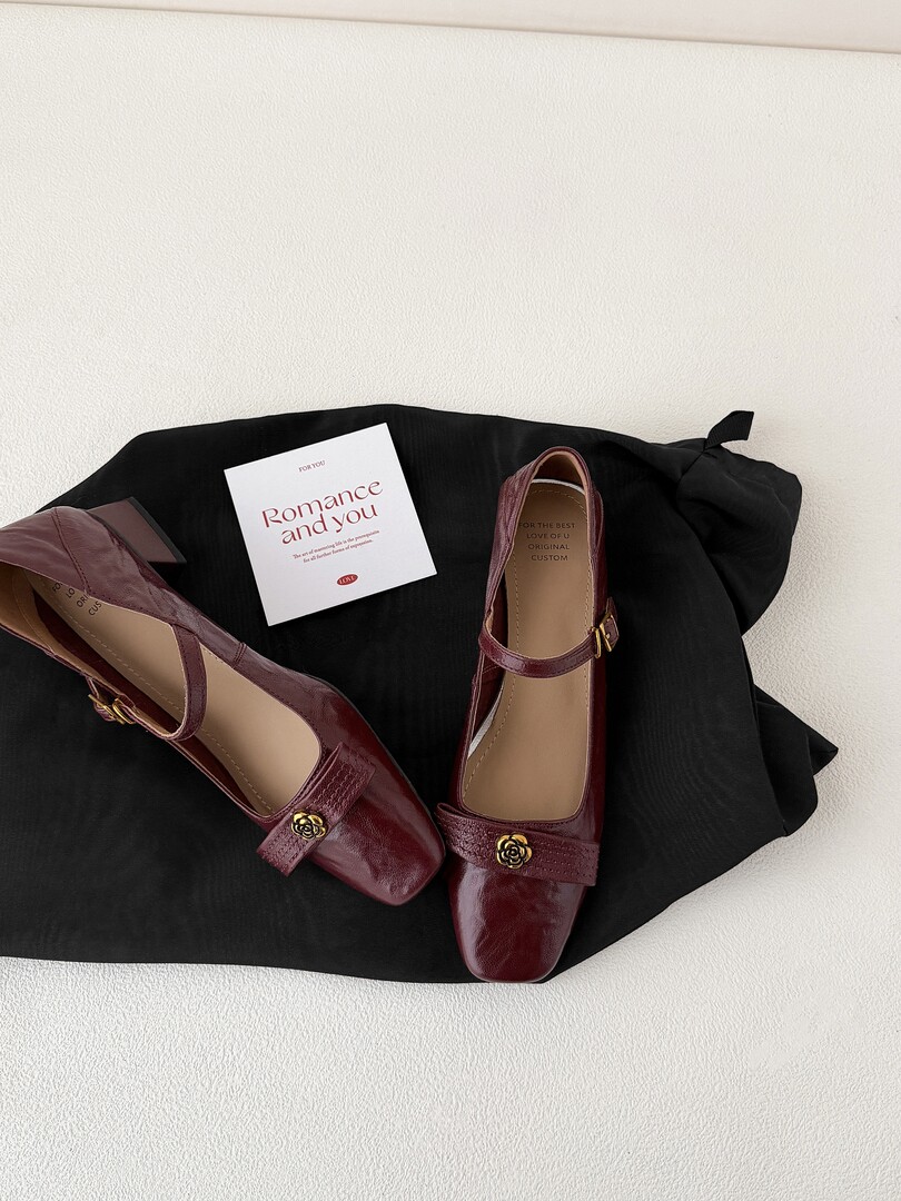 Pair of burgundy mary jane flats with decorative flower buckles on a black garment
