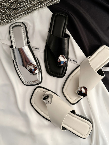 Flat slide sandals in black, white, silver, and beige displayed on fabric