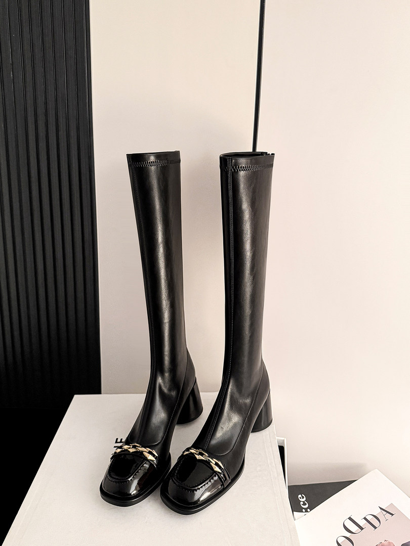 Black knee-high heeled boots with chain-accented pointed toes