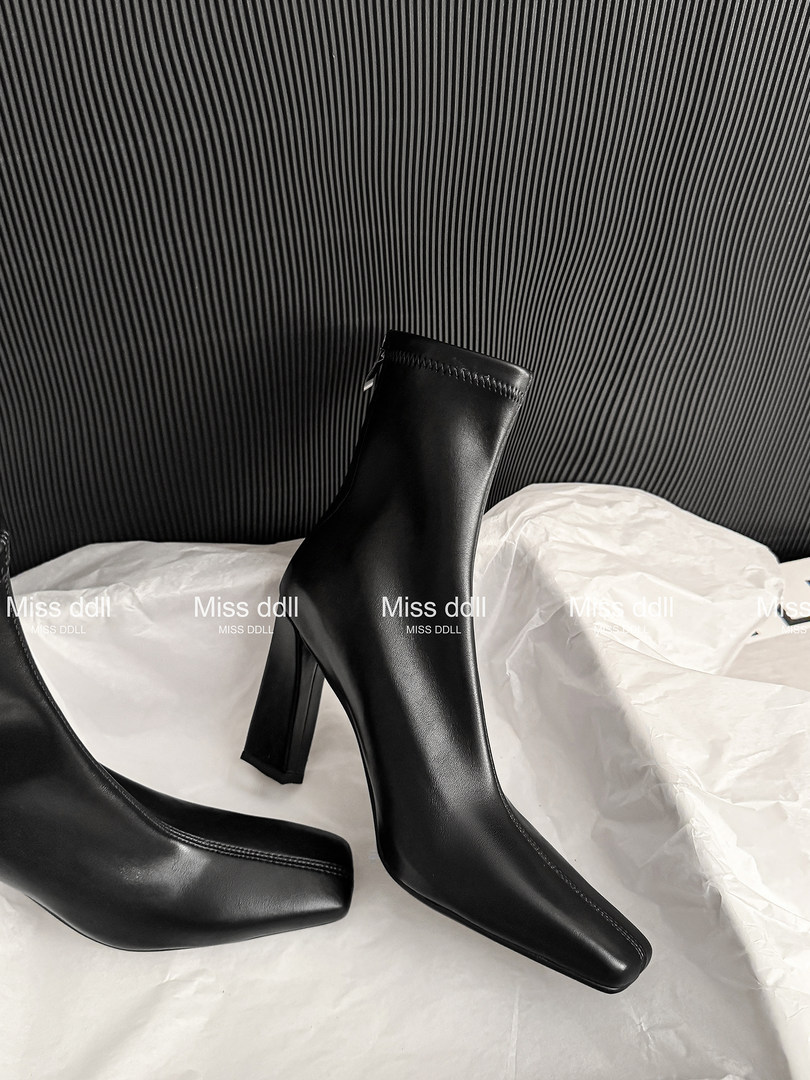 Black heeled ankle boots displayed on white tissue paper