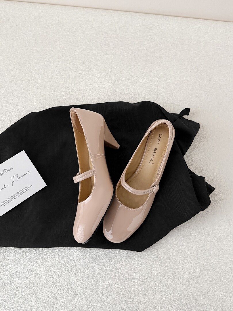 Pair of nude patent Mary Jane block-heel pumps laid flat on a black cloth