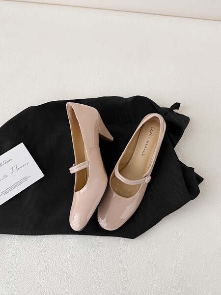 Pair of nude patent Mary Jane block-heel pumps laid flat on a black cloth