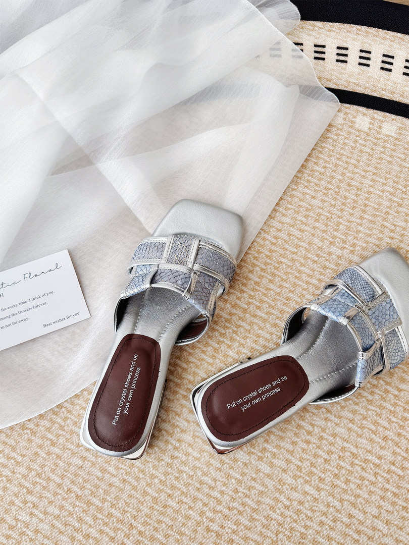 Pair of silver embellished slide sandals with a clear draped fabric background