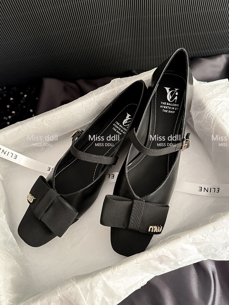Black Mary Jane-style flats with bow detail displayed on tissue paper