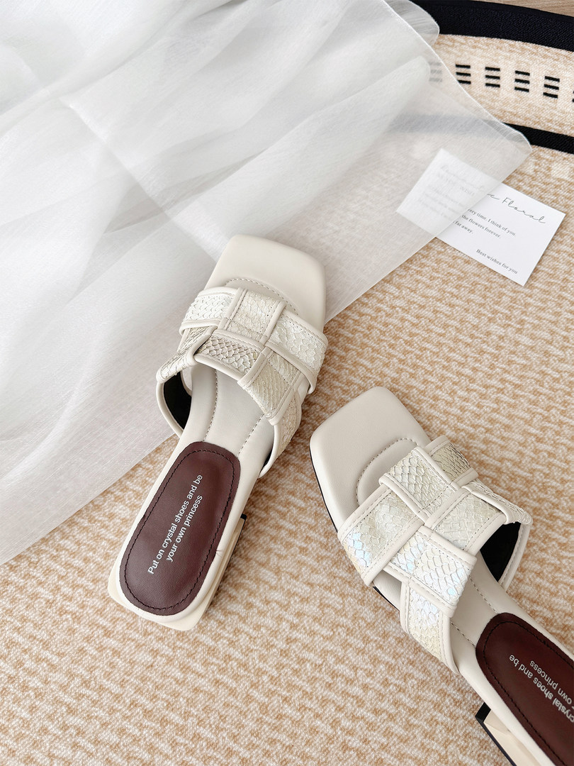 Pair of white strappy slide sandals on a textured background