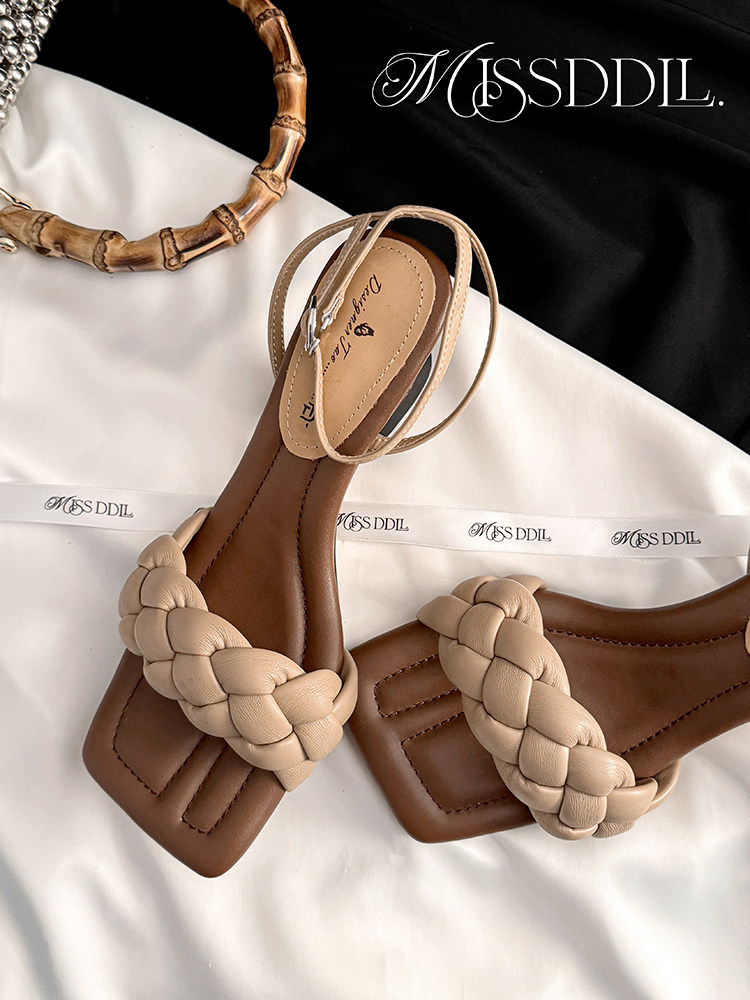 Braided beige and brown flat sandals photographed on branded fabric