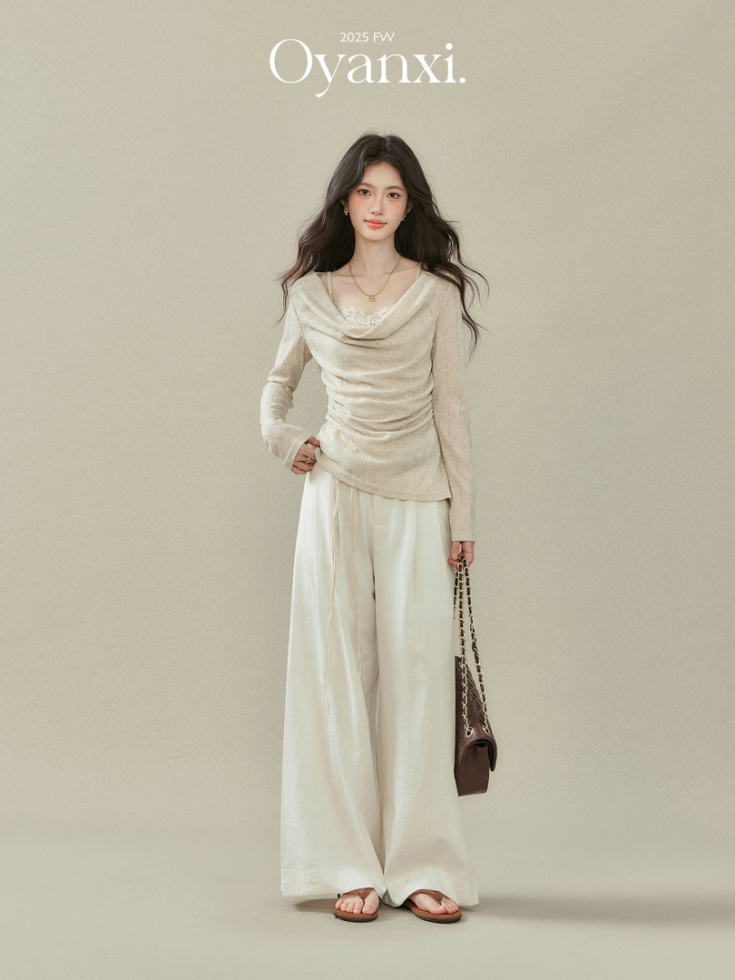 Model wearing a cream long-sleeve draped top with wide-leg pants and a brown chain-strap handbag