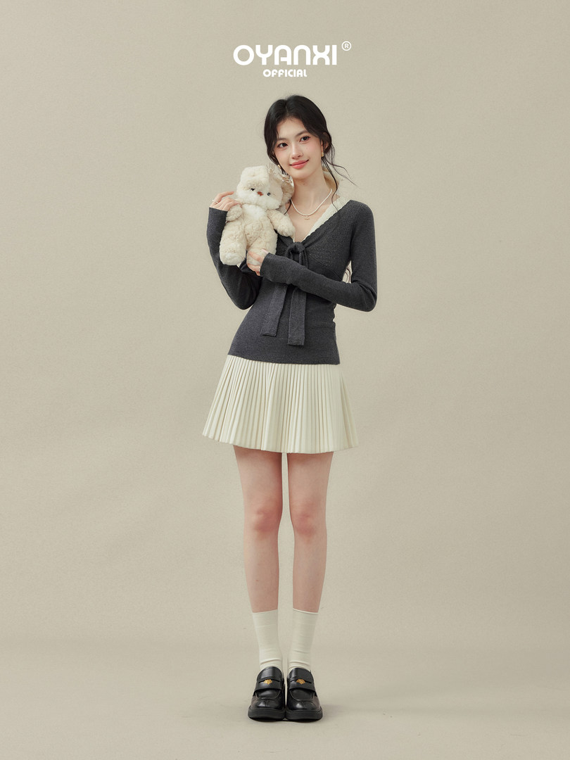 Model wearing a dark knit top and cream pleated mini skirt with loafers