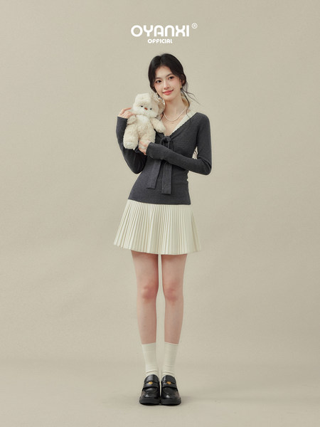 Model wearing a dark knit top and cream pleated mini skirt with loafers