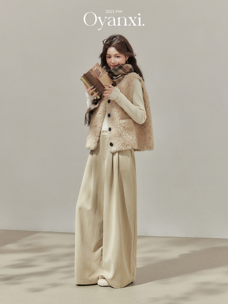 Model wearing a beige fuzzy vest, scarf, and wide-leg pants in a studio setting