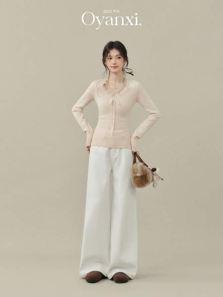 Model wearing a pale pink knit sweater with white wide-leg pants and a fur handbag