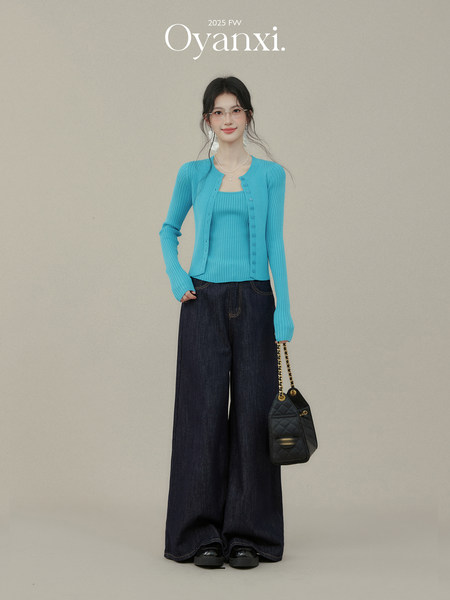 Model wearing a turquoise knit cardigan and top with wide-leg dark jeans and a black shoulder bag