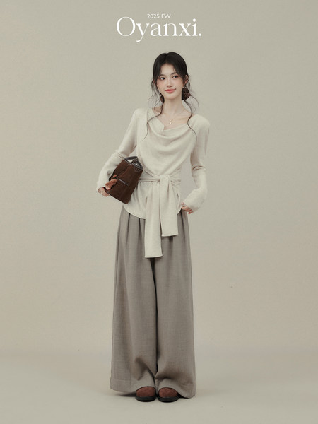 Model wearing a cream knit top and wide-leg gray pants with a brown handbag