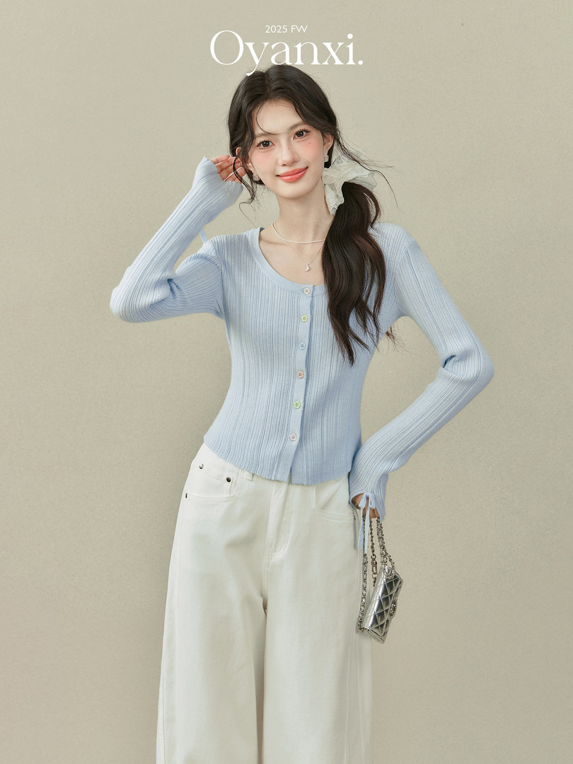 Model wearing a light blue ribbed cardigan with white wide-leg pants and a silver mini bag