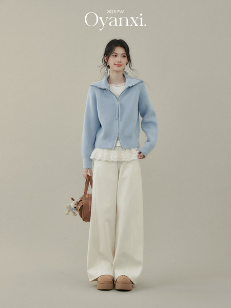 Model wearing a light blue knit cardigan with white wide-leg pants and a brown handbag