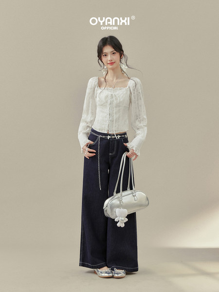 Model wearing a white lace long-sleeve blouse with dark wide-leg jeans and a silver handbag