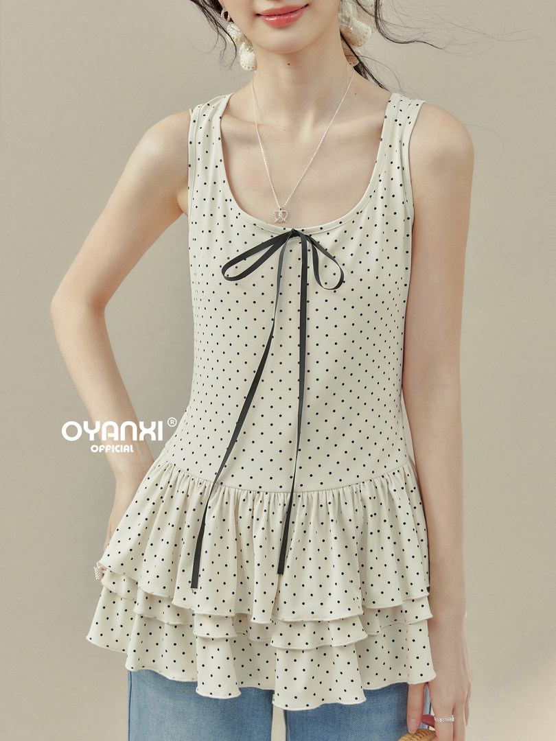 Model wearing a cream polka dot sleeveless peplum top with black ribbon tie