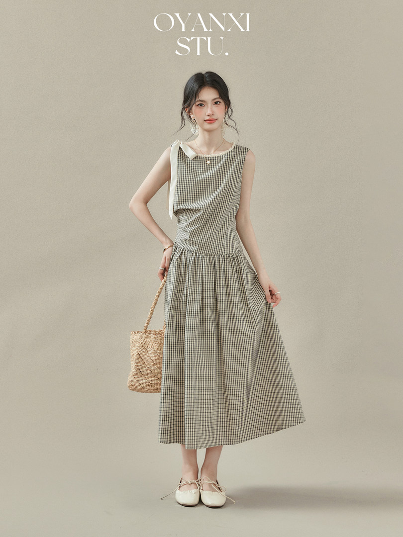 Model wearing a sleeveless checked midi dress with a woven bag and flats